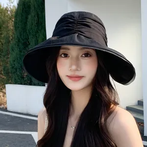 Close-up detail of a stylish pleated black sun hat worn by a female model in outdoor sun