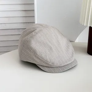 Gros plan d'une casquette gavroche grise à rayures rétro posée sur une table blanche.