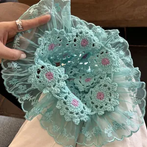 Close-up of mint green handmade crochet beanie with purple floral centers and lace edge.