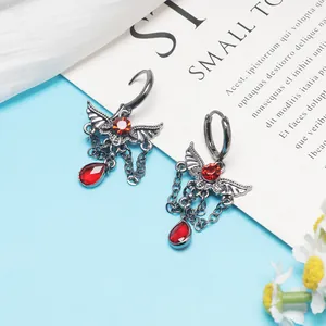 Macro detail view showing gothic wing earrings with red drop crystals and chains.
