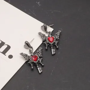 Macro detail view of gothic heart key earrings featuring red crystals and dark metal wings