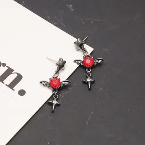 Close-up of gothic blood moon earrings with red gems, wings, and cross pendants.