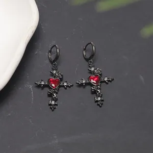 Detail view of gothic black cross earrings featuring a central red heart-shaped gemstone.