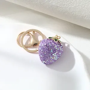 Close-up detail of purple rhinestone strawberry keychain with gold hardware on a white plate