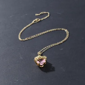 Close-up view of a gold thorn rose heart necklace with a sparkling pink pendant gemstone.