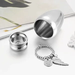 Close-up of egg-shaped metal memorial urn with angel wing charm and beaded ring