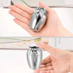 Detail view of a small stainless steel memorial urn with angel wing charm held in hand.