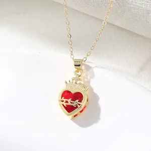 Detailed view of a gold Sacred Heart pendant featuring a red stone and cross design.