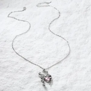 Close-up detail of a silver spider pendant featuring a heart-shaped pink crystal jewel