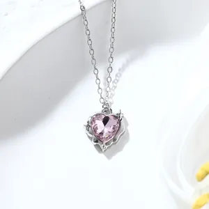Macro detail of silver heart necklace with sparkling pink gemstone and cross motifs