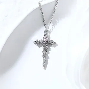 Close-up of silver-tone cross necklace with pink heart crystal and delicate rose details.