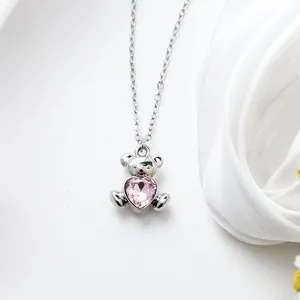 Close-up detail of a silver-tone teddy bear necklace holding a sparkling pink heart crystal.