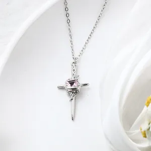 Close-up detail of a silver-toned textured cross pendant with a pink square crystal