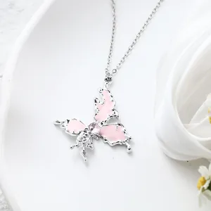 Macro detail of a silver butterfly pendant with pink enamel and a central pink heart gemstone
