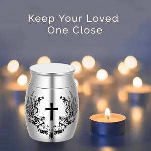 Kleine silberne Urne mit Kreuz- und Engelsflügel-Gravur vor Kerzenhintergrund