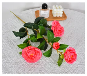 Close-up of artificial pink camellia branch with green leaves on white tablecloth