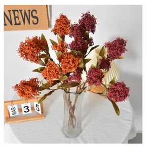 Close-up of artificial Skimmia japonica berries in orange and red in glass vase.