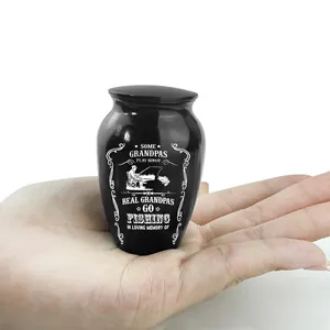 Miniature black cremation urn for grandpa with fishing design shown in hand for scale