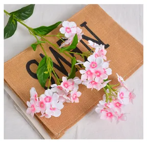 Close-up of artificial white Phlox flowers with pink centers on a jute background.