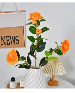 Detailed view of a vibrant orange artificial camellia branch in a white decorative vase