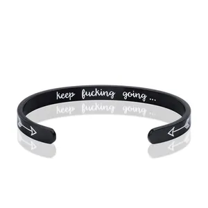 Gros plan du bracelet en acier noir avec gravure keep fucking going et flèche.
