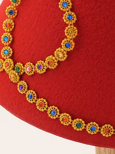 Close-up detail showing multi-colored gemstones and gold floral trim on ethnic red felt hat