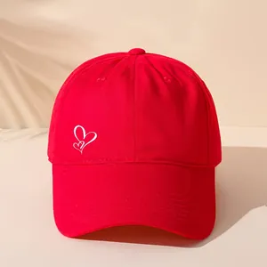 Detailansicht einer roten Baseballkappe mit einer weißen Doppelherz-Stickerei an der Seite.