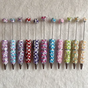 Row of colorful beaded ballpoint pens with butterfly decorations on a white texture.