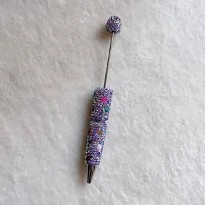 Macro view of handmade pen featuring purple rhinestones and colorful stone accents.