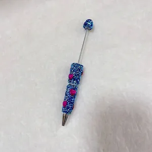 Close-up detail of a handmade blue rhinestone ballpoint pen with charming pink hearts.