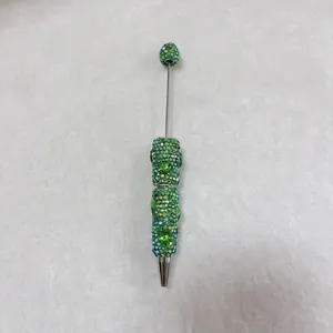 Macro detail of a handmade green rhinestone beaded pen on soft grey textured felt