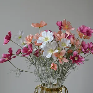 Close-up detail of mixed color artificial cosmos flowers arranged in a gold vase
