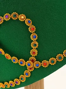Close-up macro detail of colorful gemstones on golden trim of exotic green felt hat