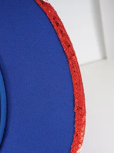 Détail macro montrant des paillettes rouges et un tissu bleu texturé sur un chapeau