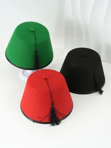 Detalle de gorros Fez rojos, verdes y negros con borlas negras sobre fondo blanco.