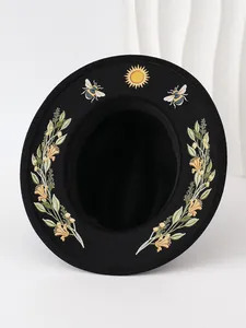 Detailed view of the sun and bee embroidery patterns on a black gothic fedora hat.