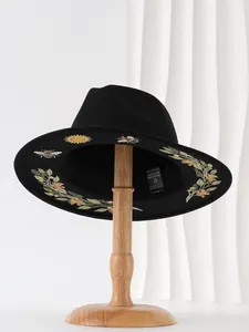 Gothic black fedora hat with floral and sun embroidery details on a wooden hat stand.