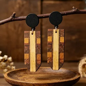 Primo piano di orecchini a pendente in legno a strisce retrò su sfondo di rami rustici.