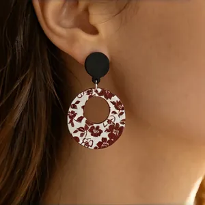 Close-up detail of vintage round wooden hoop earrings with red floral print on a model's ear.