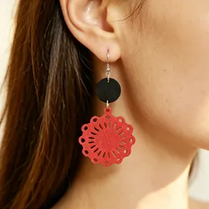 Dettaglio di orecchini vintage in legno rosso con motivo floreale tradizionale su modella.