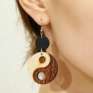 Primo piano di orecchini pendenti in legno Yin Yang con design traforato indossati sull'orecchio