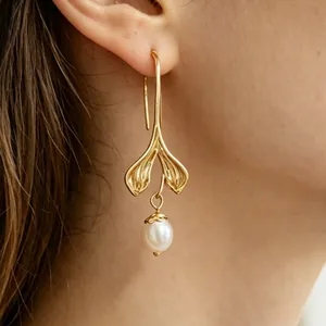 Primer plano de pendientes dorados con forma de cola de sirena y perla blanca.
