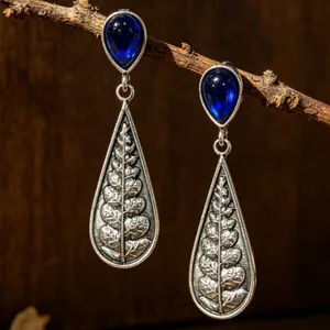 Close-up of vintage waterdrop earrings with intricate silver fern leaf patterns and blue stones