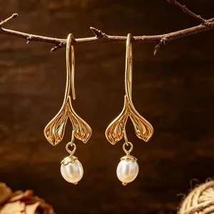 Elegantes pendientes dorados de cola de sirena con perlas blancas en una rama de madera rústica.