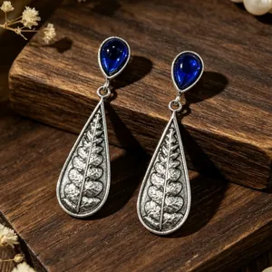 Macro view of vintage teardrop earrings with sapphire blue stones and fern engraving.