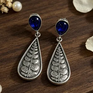 Detailed macro view of vintage teardrop earrings with blue gems and fern leaf engravings