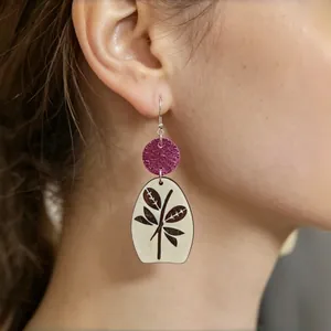 Primer plano de elegantes pendientes de madera con purpurina fucsia y estampado de hojas