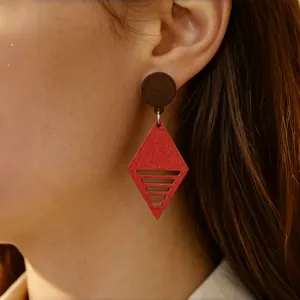 Dettaglio di orecchini geometrici in legno con pendente a rombo rosso sull'orecchio