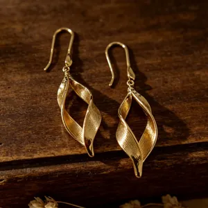 Detalle de pendientes dorados en espiral con textura de rayas verticales sobre madera