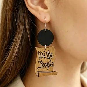 Dettaglio della calligrafia We the People su un orecchino pendente in legno vintage.